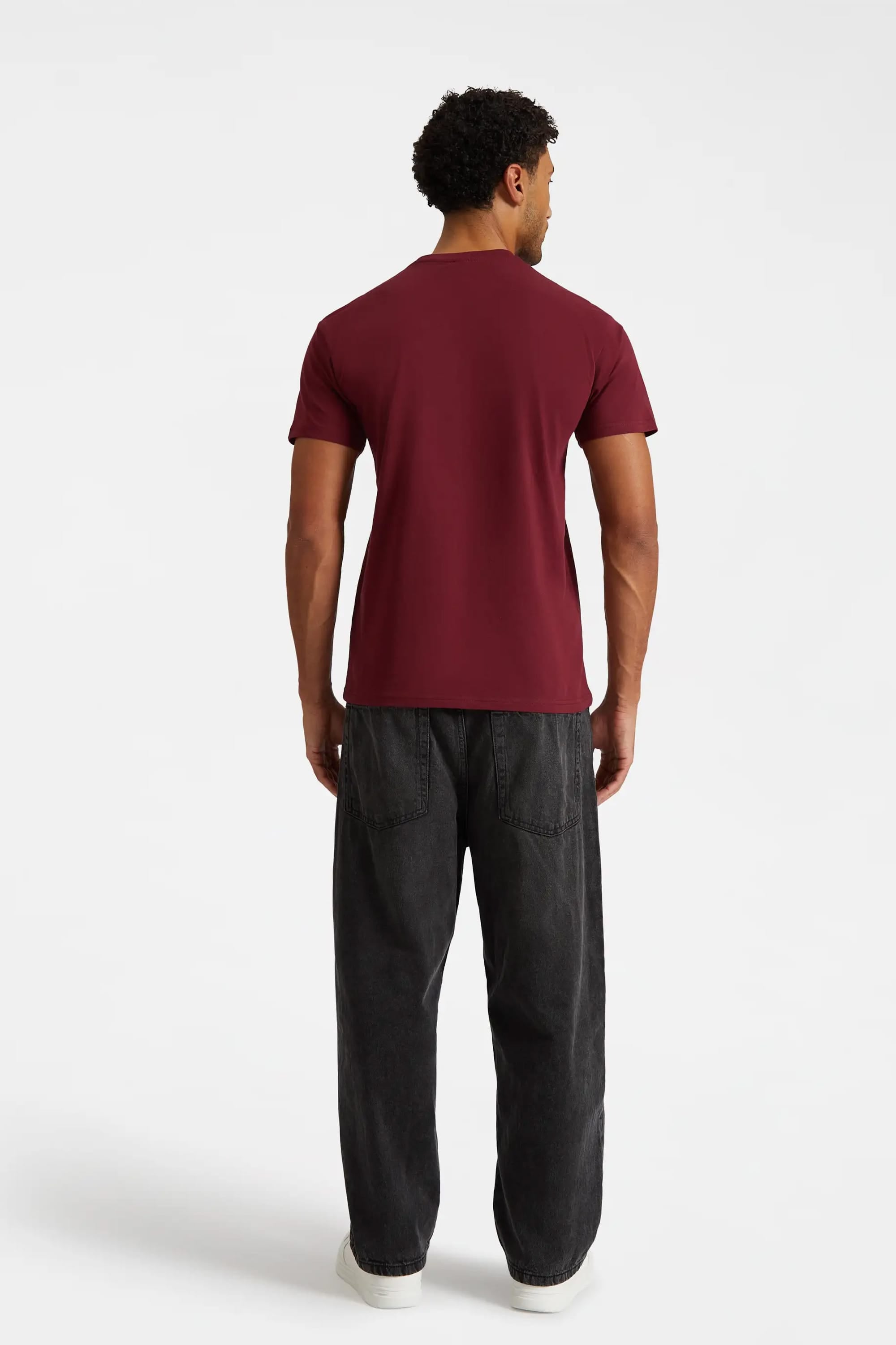 Man wearing a maroon t-shirt and dark pants on a white background