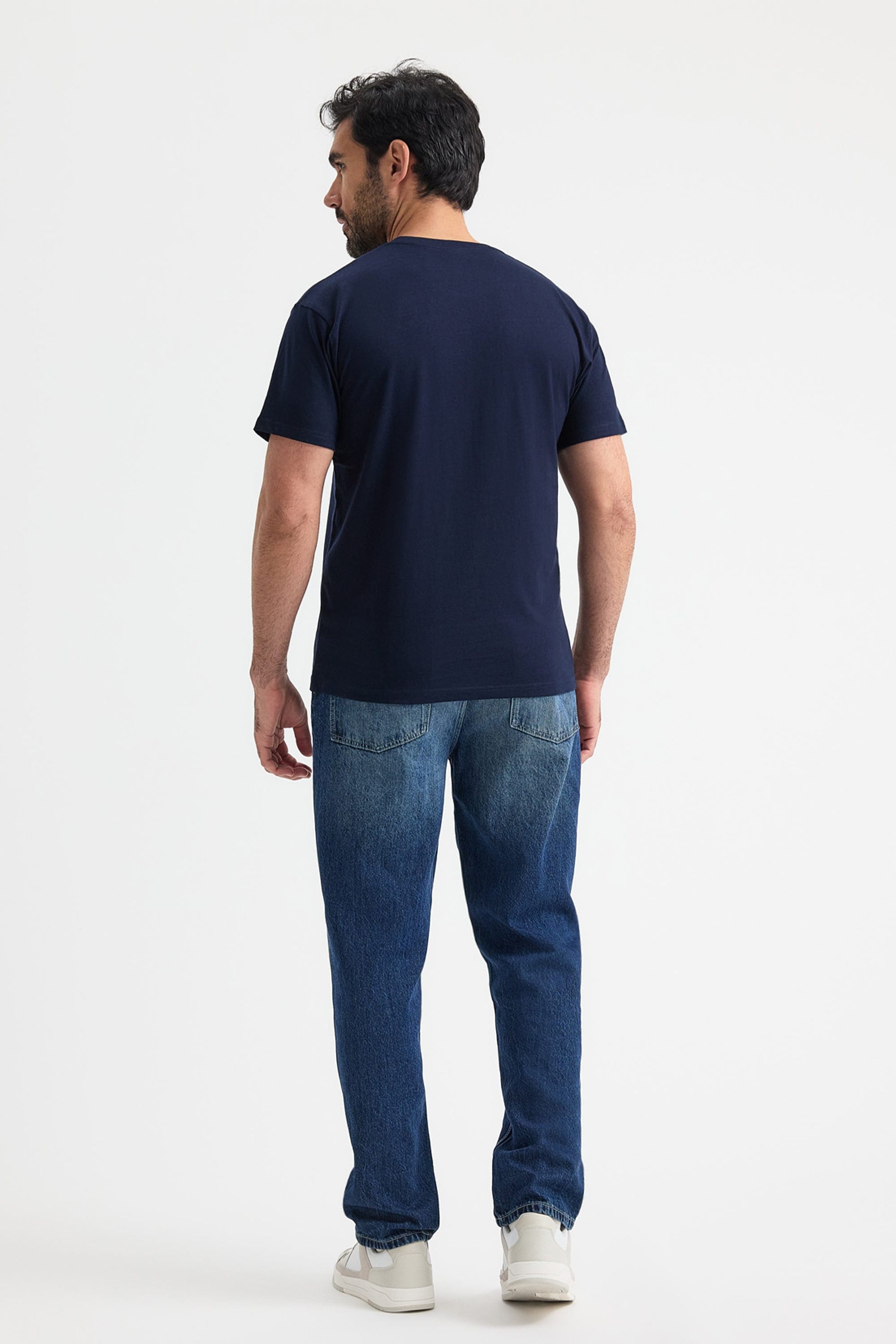 Man wearing a navy blue t-shirt and blue jeans on a white background