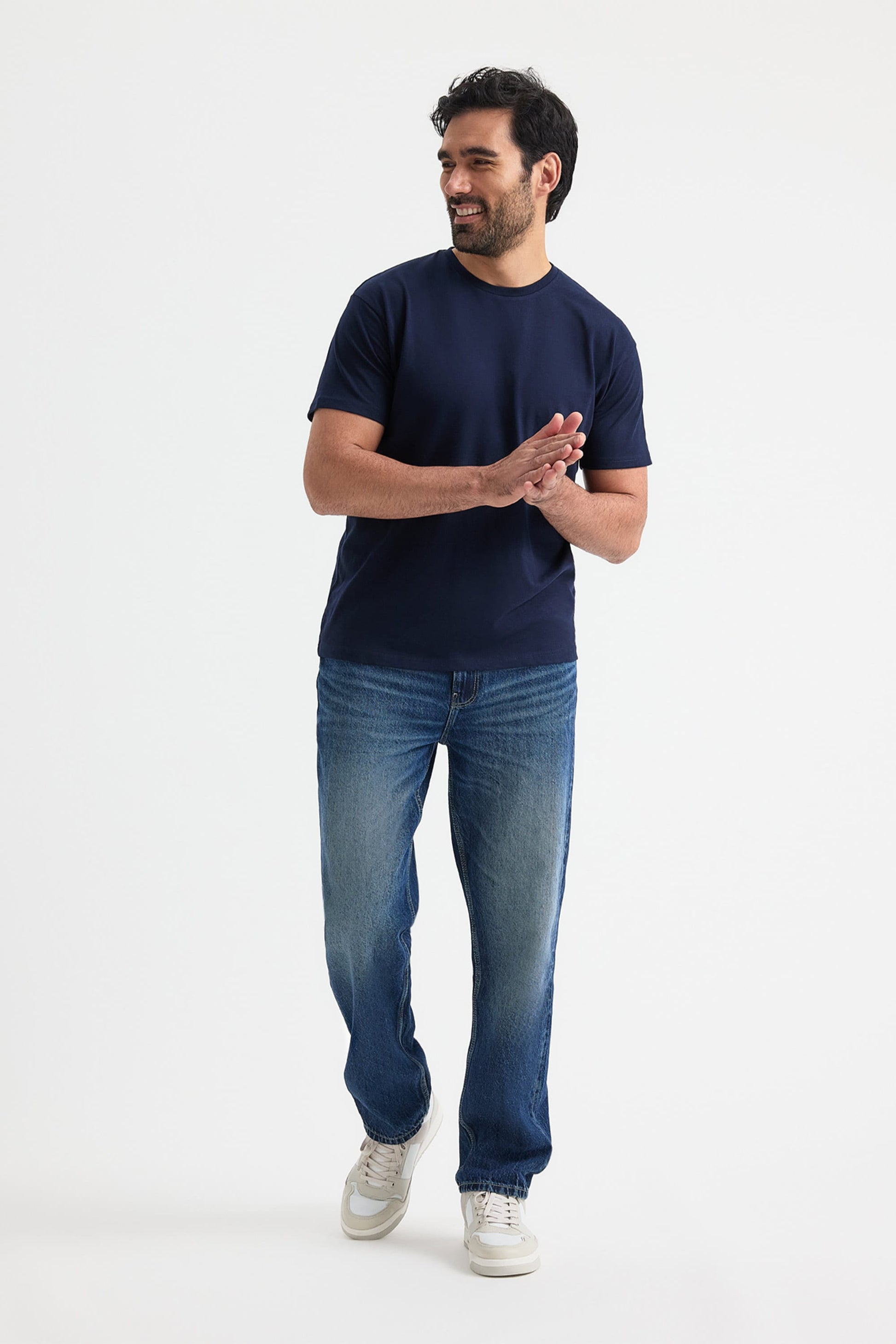 Man wearing a navy t-shirt and blue jeans standing on a white background
