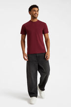 Man wearing a burgundy t-shirt and black pants on a white background