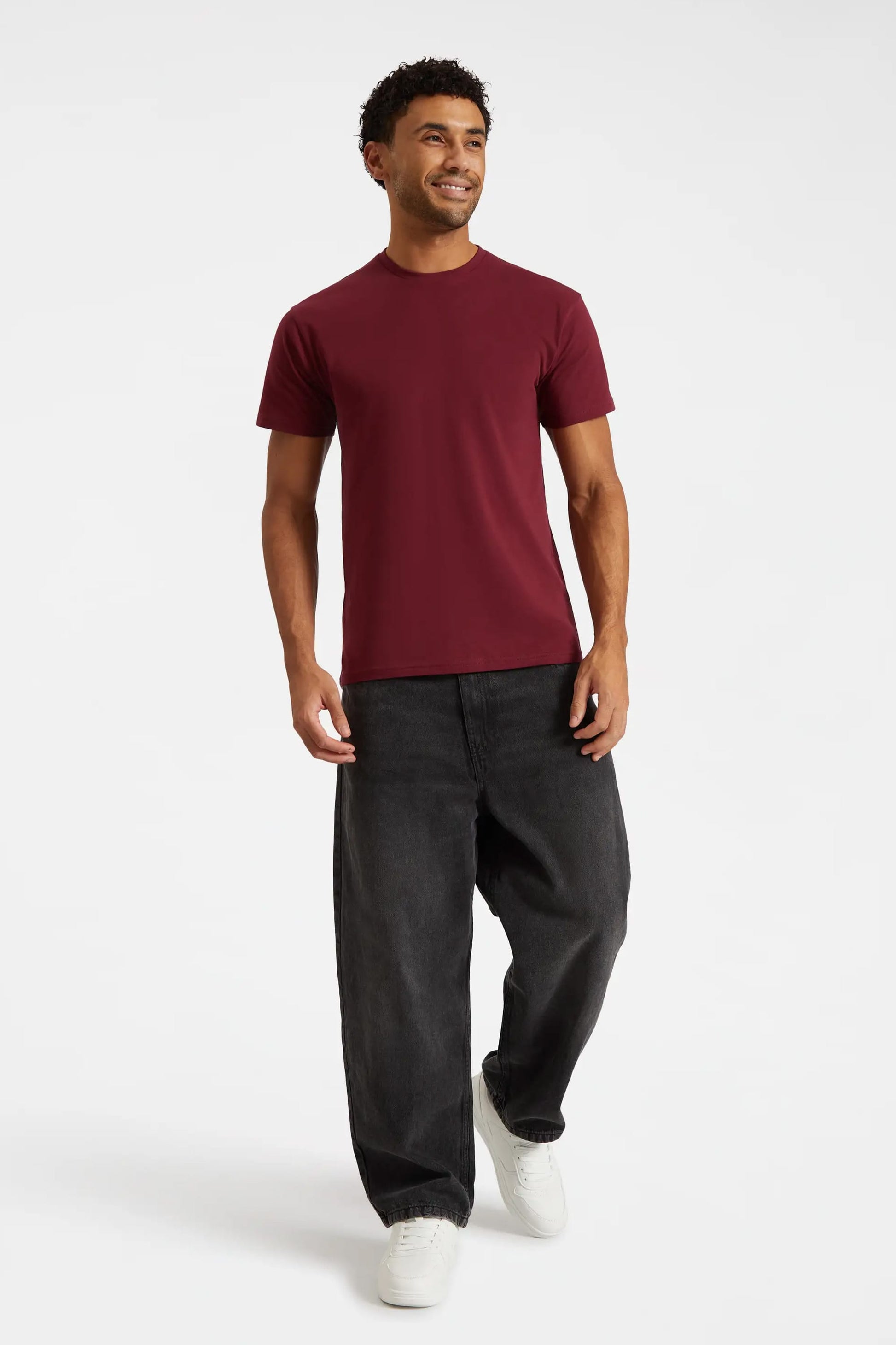 Man wearing a burgundy t-shirt and black pants on a white background
