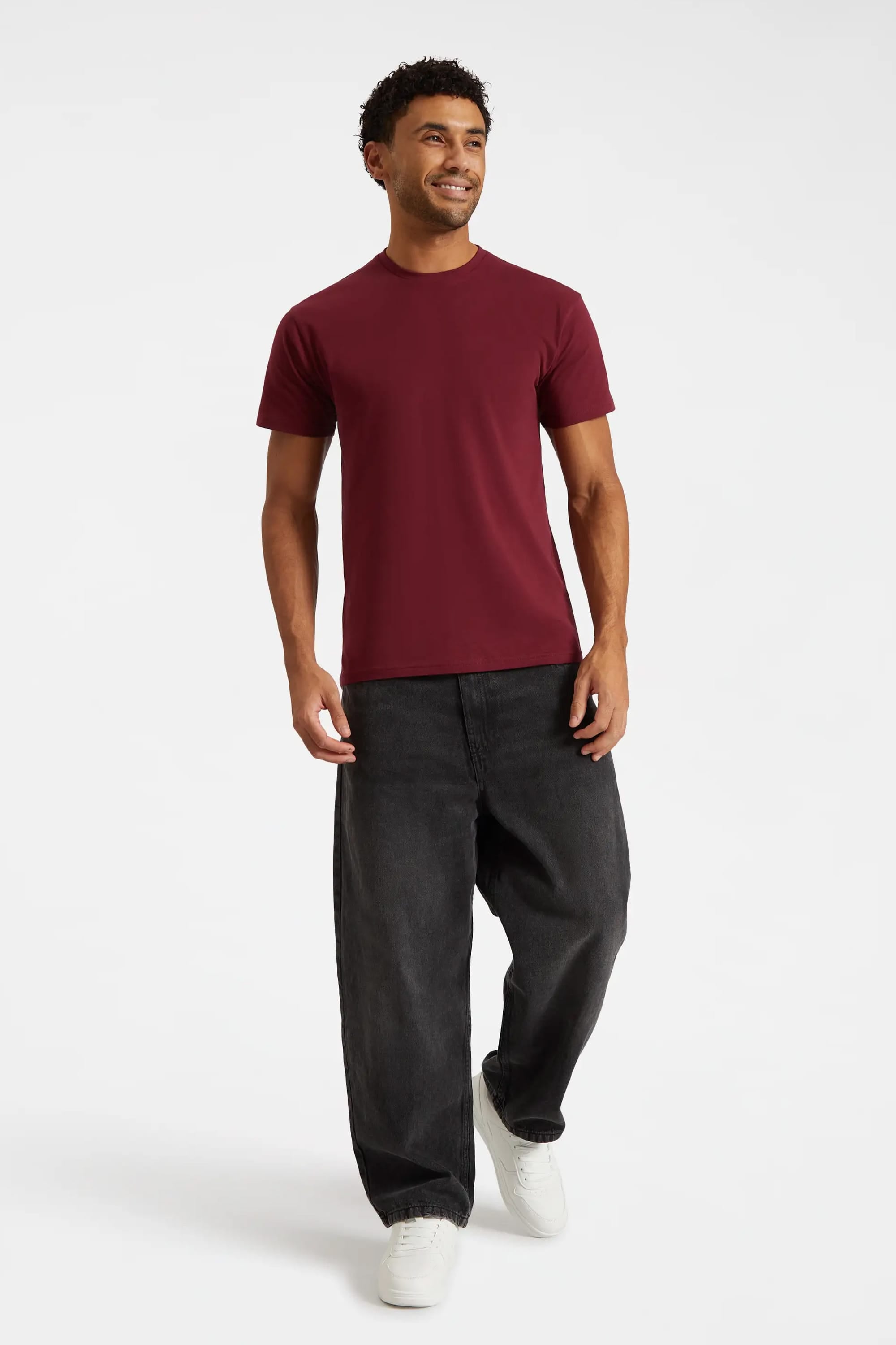 Man wearing a burgundy t-shirt and black pants on a white background
