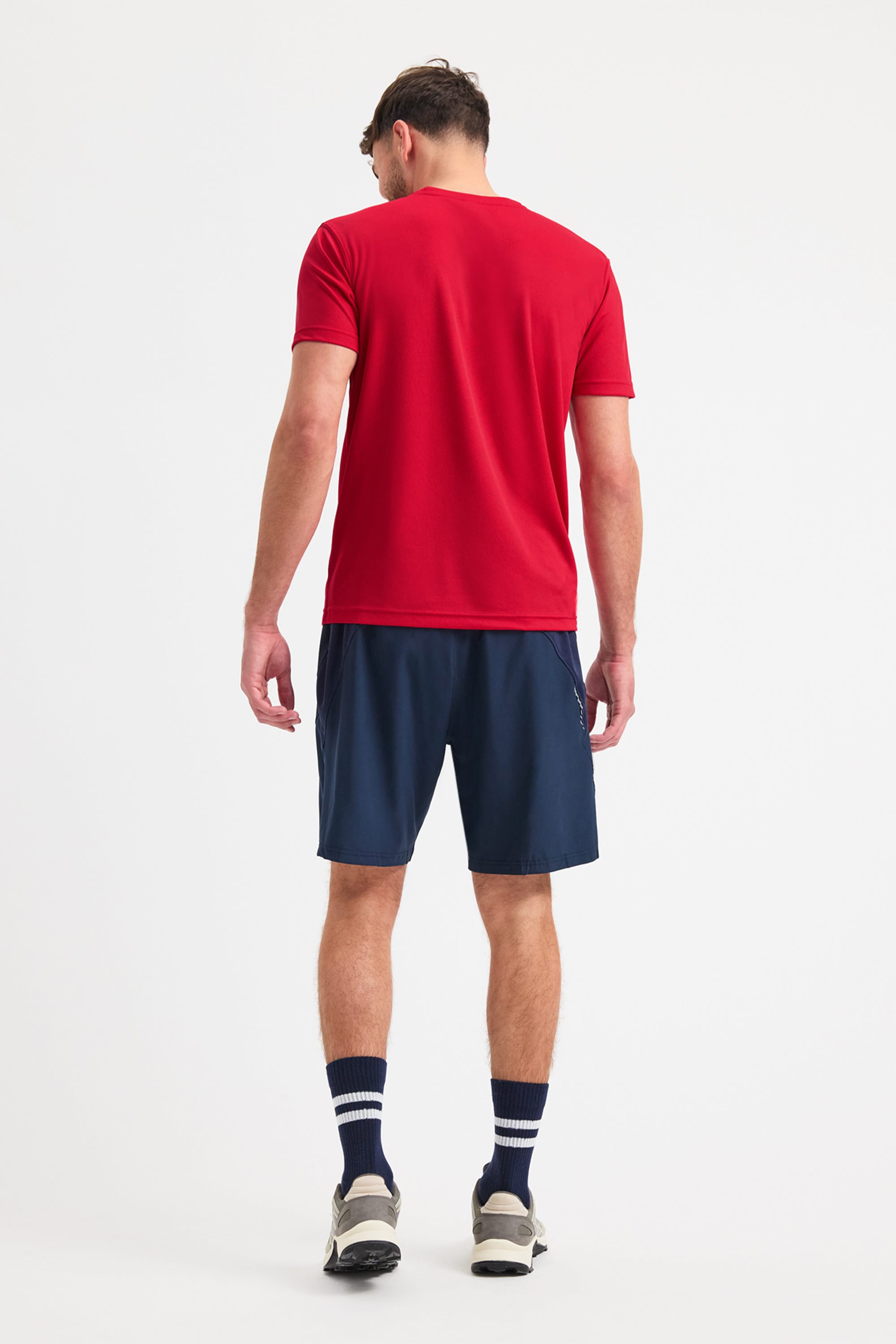 Man wearing a red t-shirt and navy shorts on a white background